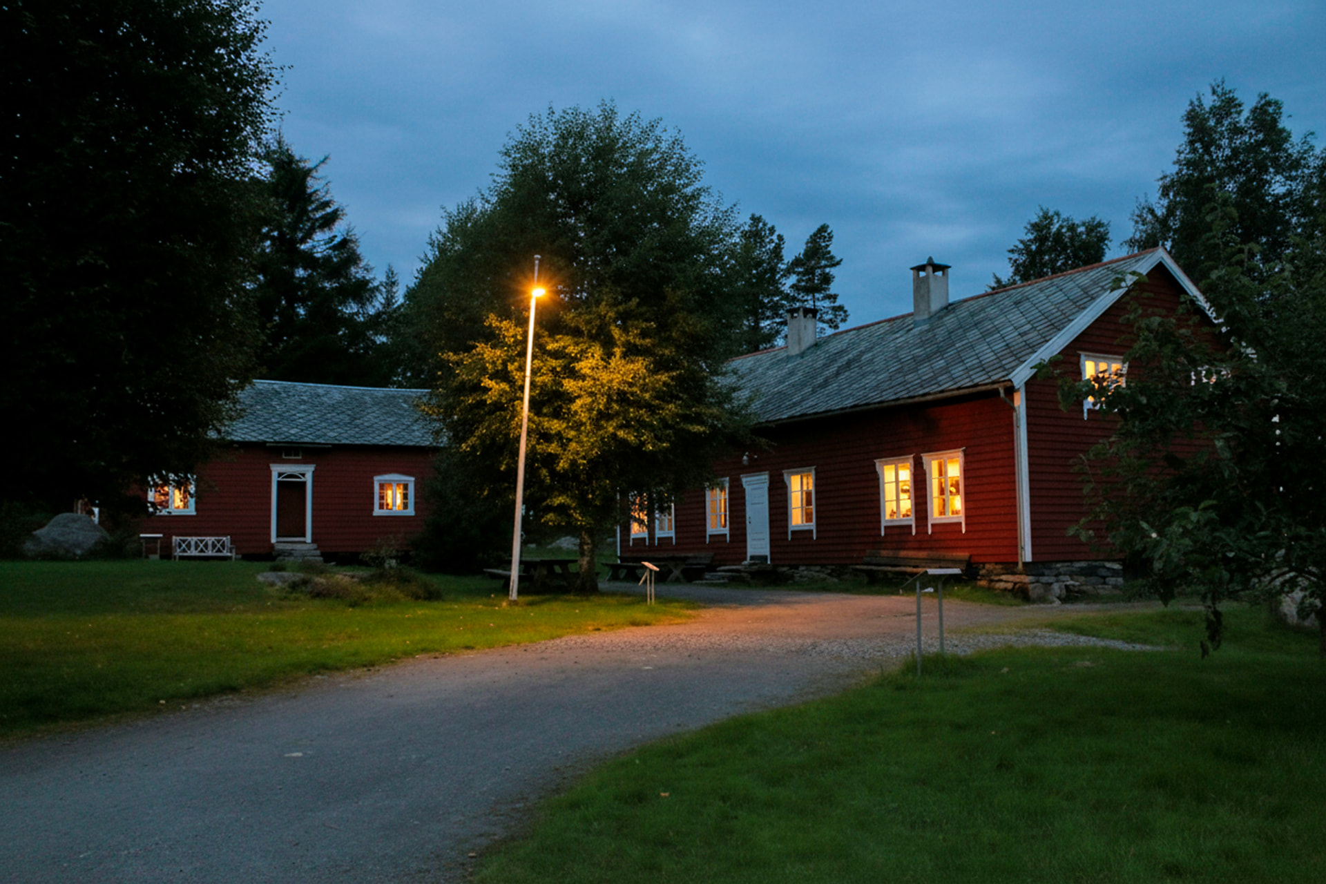 Röd stuga i skymning med varmt ljus i fönstren